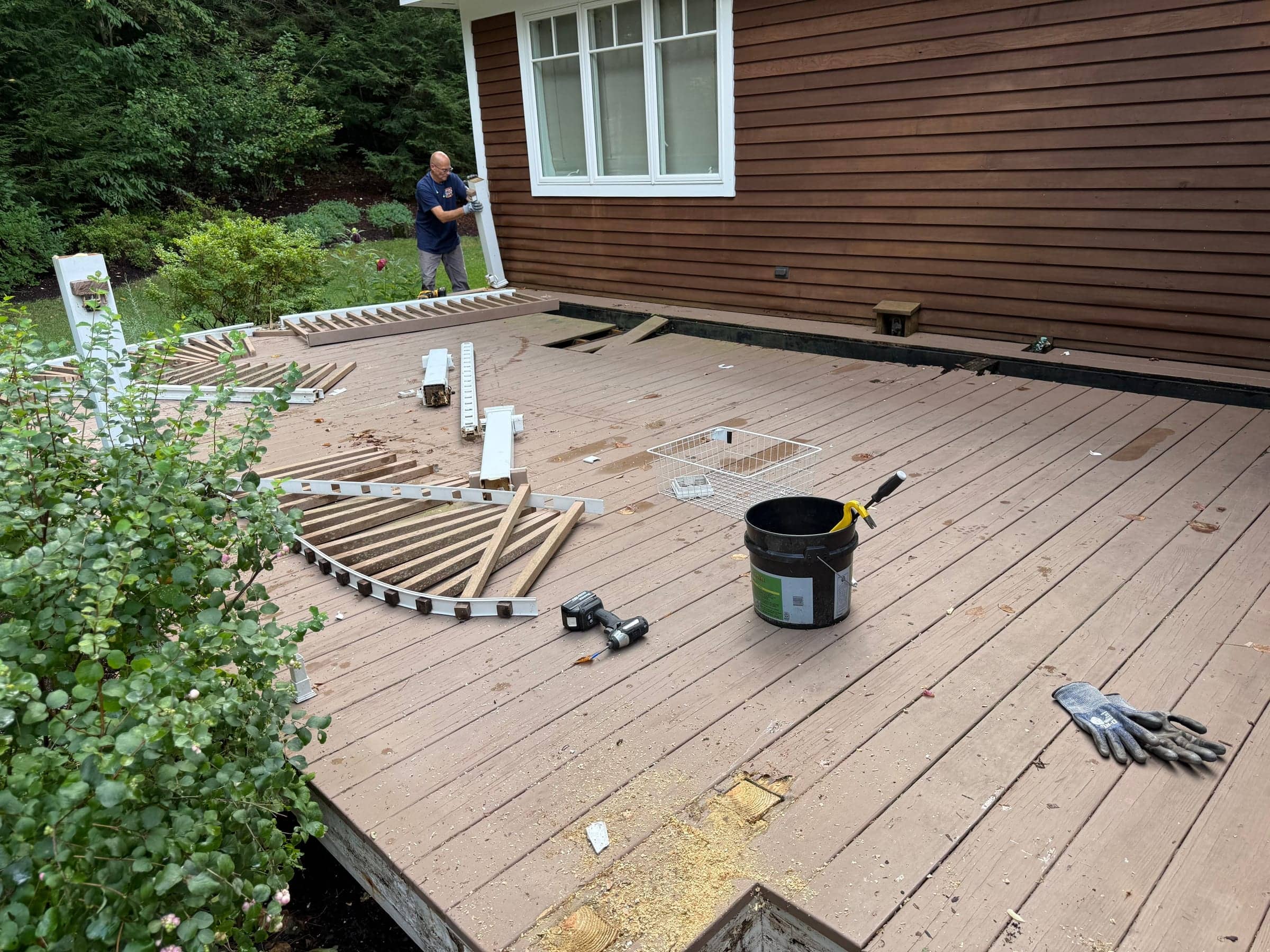 A McWain crew member pulling up deck railings, with railing sections and tools laid out on the deck boards